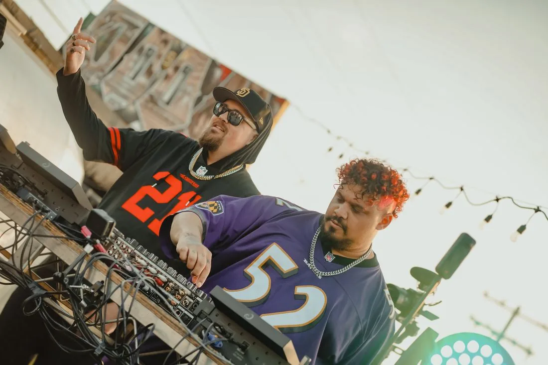 Two DJs at the decks seen from below, one in a number 52 jersey