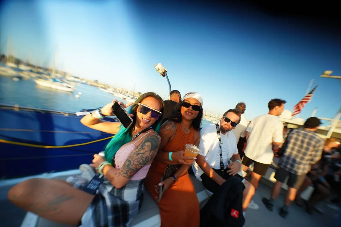 Crowd on the open deck in daylight with boats and the bay behind